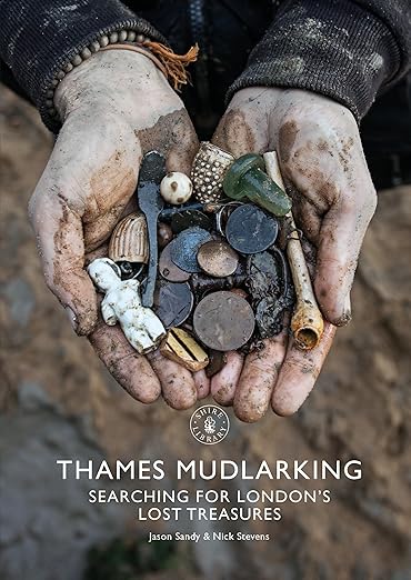 A pair of muddy hands holding various historical artifacts found on the River Thames, including coins and other small items.